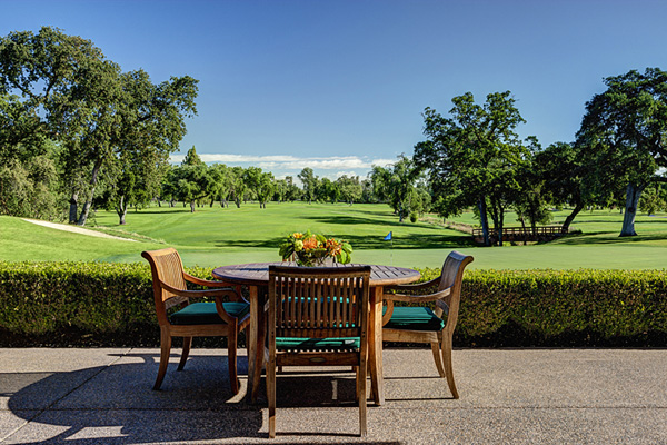 Outdoor patio with wooden table and chairs overlooking a green golf course, sunny calm mood